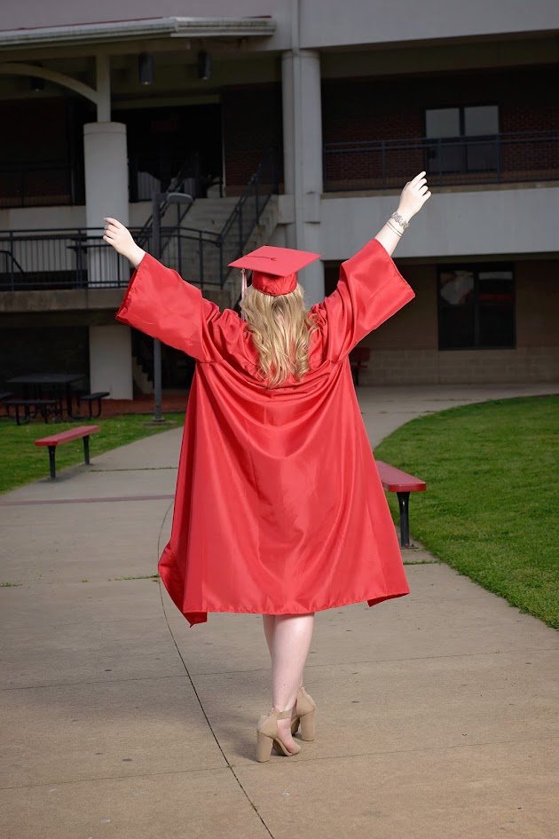 Jess in a red graduation gown with her arms raised